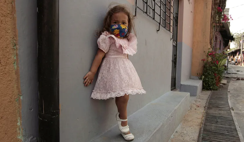 ילדה קטנה בשמלה ורודה נשענת על קיר ברחוב